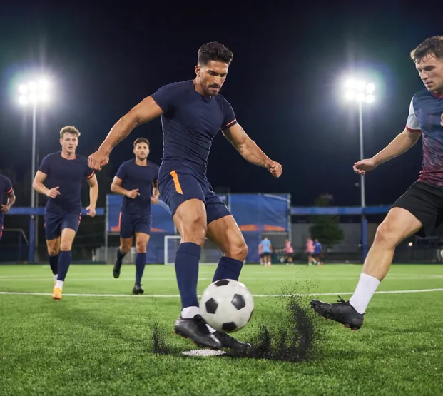 Adult league soccer player striking the ball under stadium floodlights at night